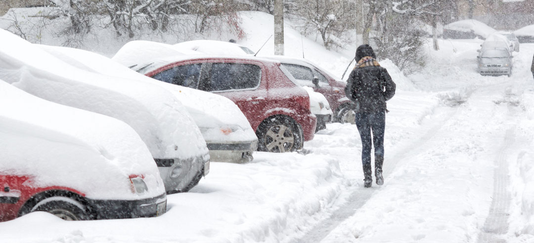 Mujer andando por una calle completamente nevada con coches