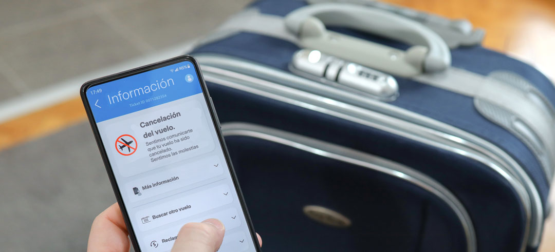 Móvil mostrando información sobre la cancelación de un vuelo con maleta de fondo