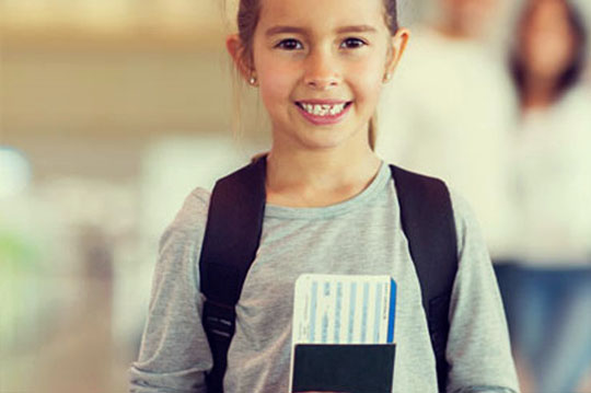 Niña pequeña sonriendo con mochila y el pasaporte de la mano